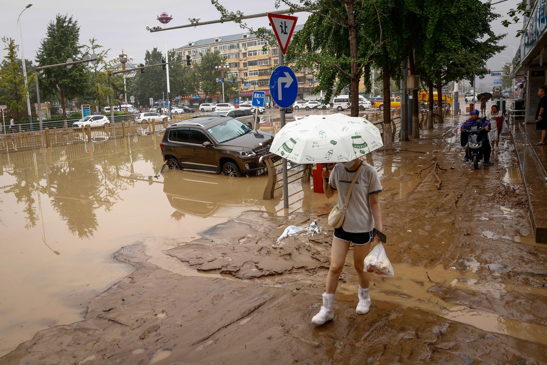 A woman walks on a muddy street next to damaged by flood cars during a downpour in Mentougou District, west of Beijing, China, 01 August 2023. EFE-EPA/MARK R. CRISTINO