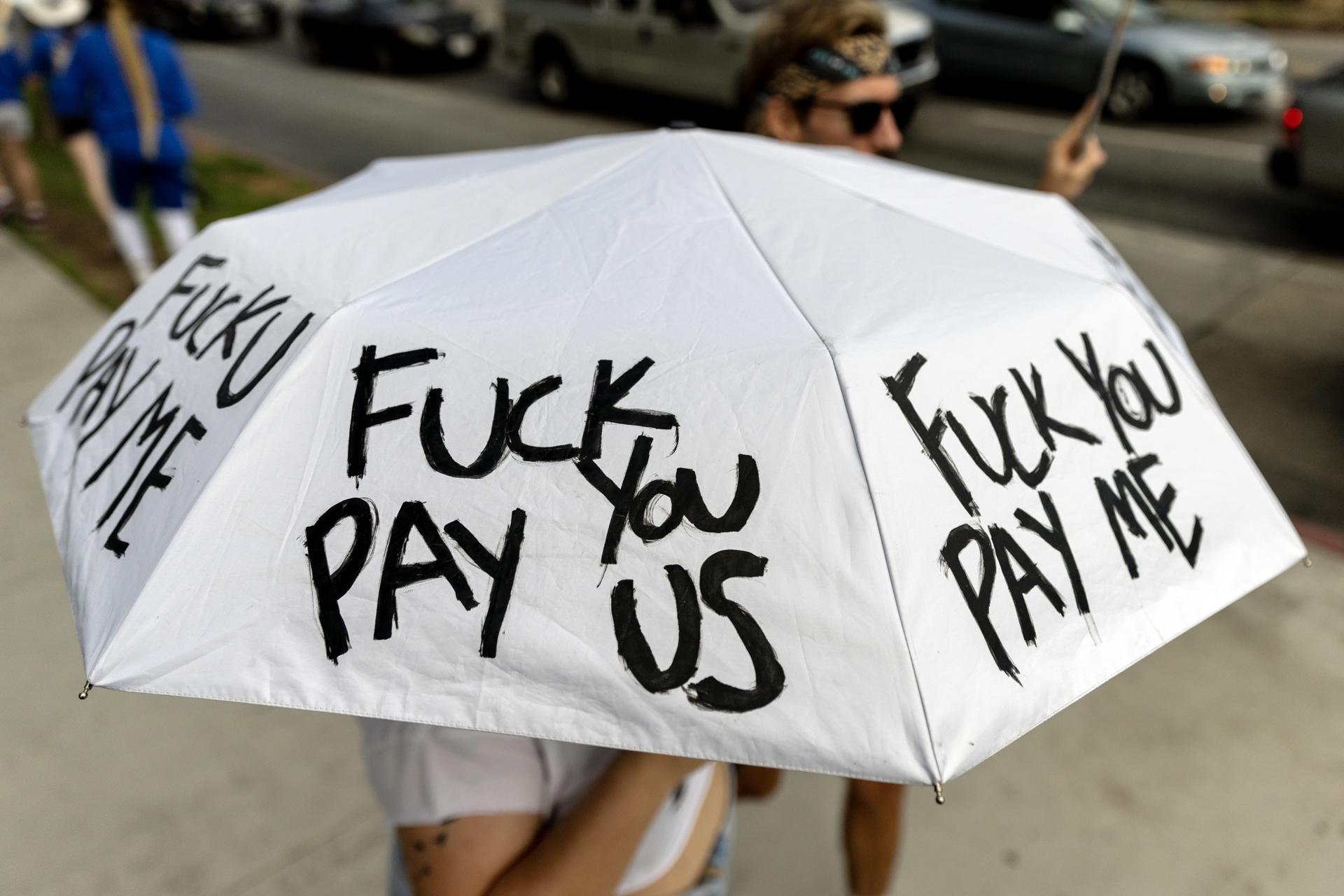 A demonstrator holds an umbrella reading 'Fuck you pay us' as members of the Writers Guild of America (WGA) protest in front of the Netflix headquarter in Los Angeles, California, USA, 09 August 2023. EFE-EPA/ETIENNE LAURENT/FILE
