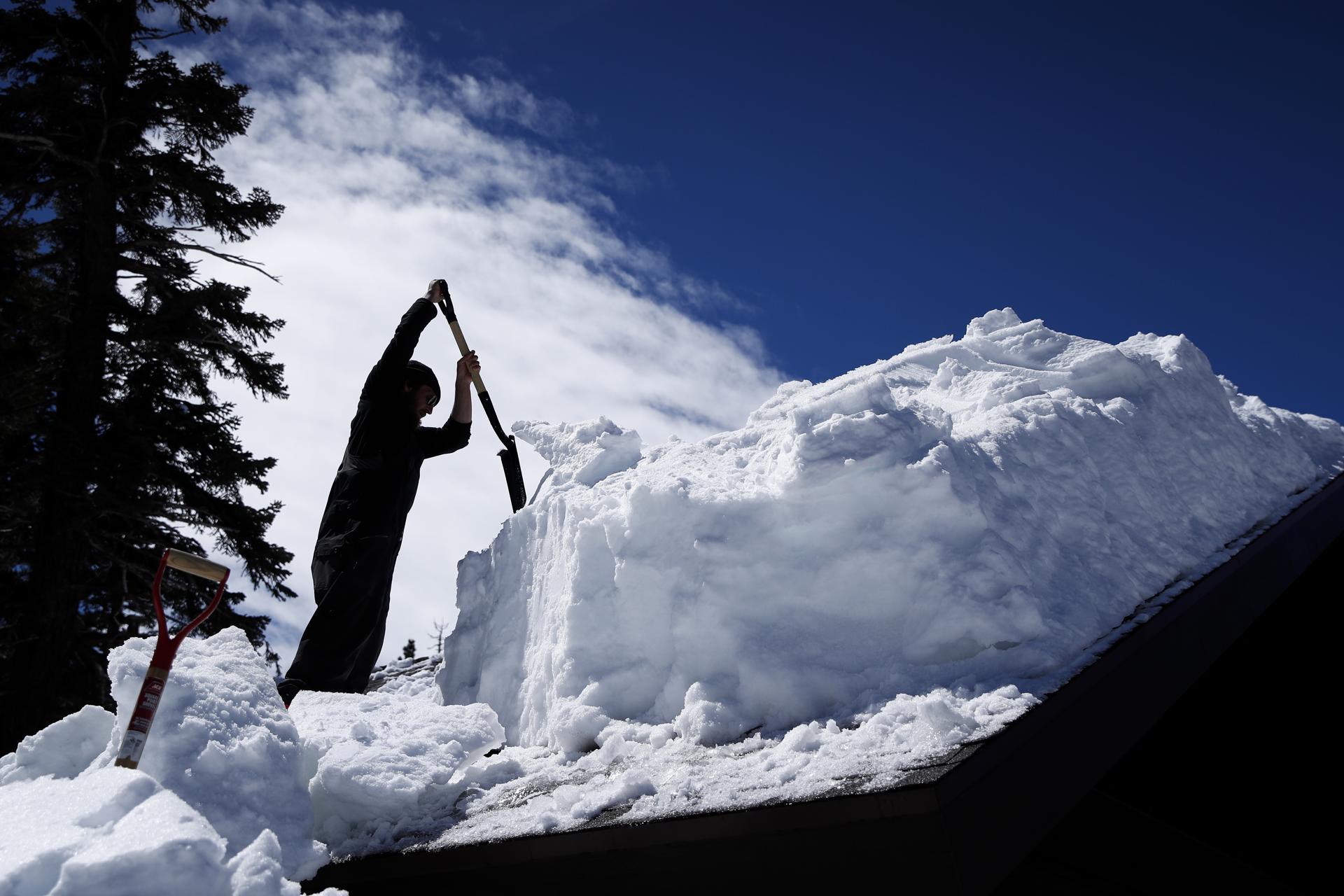 Fotografía de archivo de un hombre quitando hielo del techo de una casa después de una tormenta. EFE/Caroline Brehman