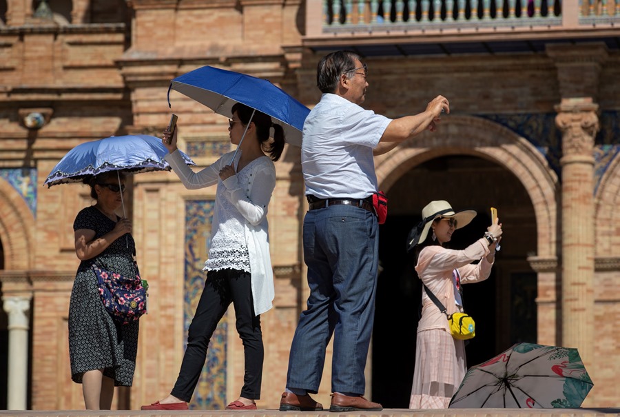 Unos turistas asiáticos se protegen del sol en la Plaza de España de Sevilla. 