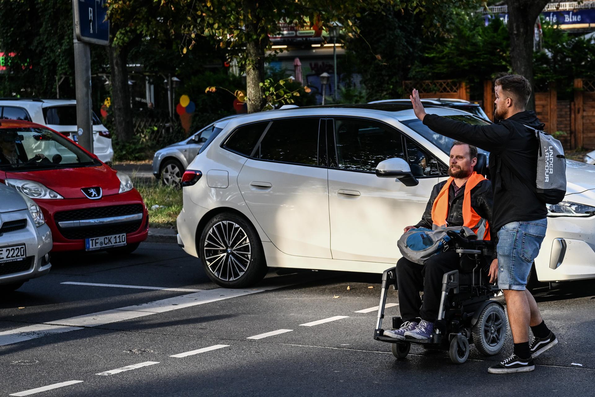 A police officer (R) in mufti gestures to stop drivers as he arrests an activist, on a motorised wheelchair, of the Last Generation climate activism group from a street in Berlin, Germany, 18 September 2023. EFE/EPA/FILIP SINGER
