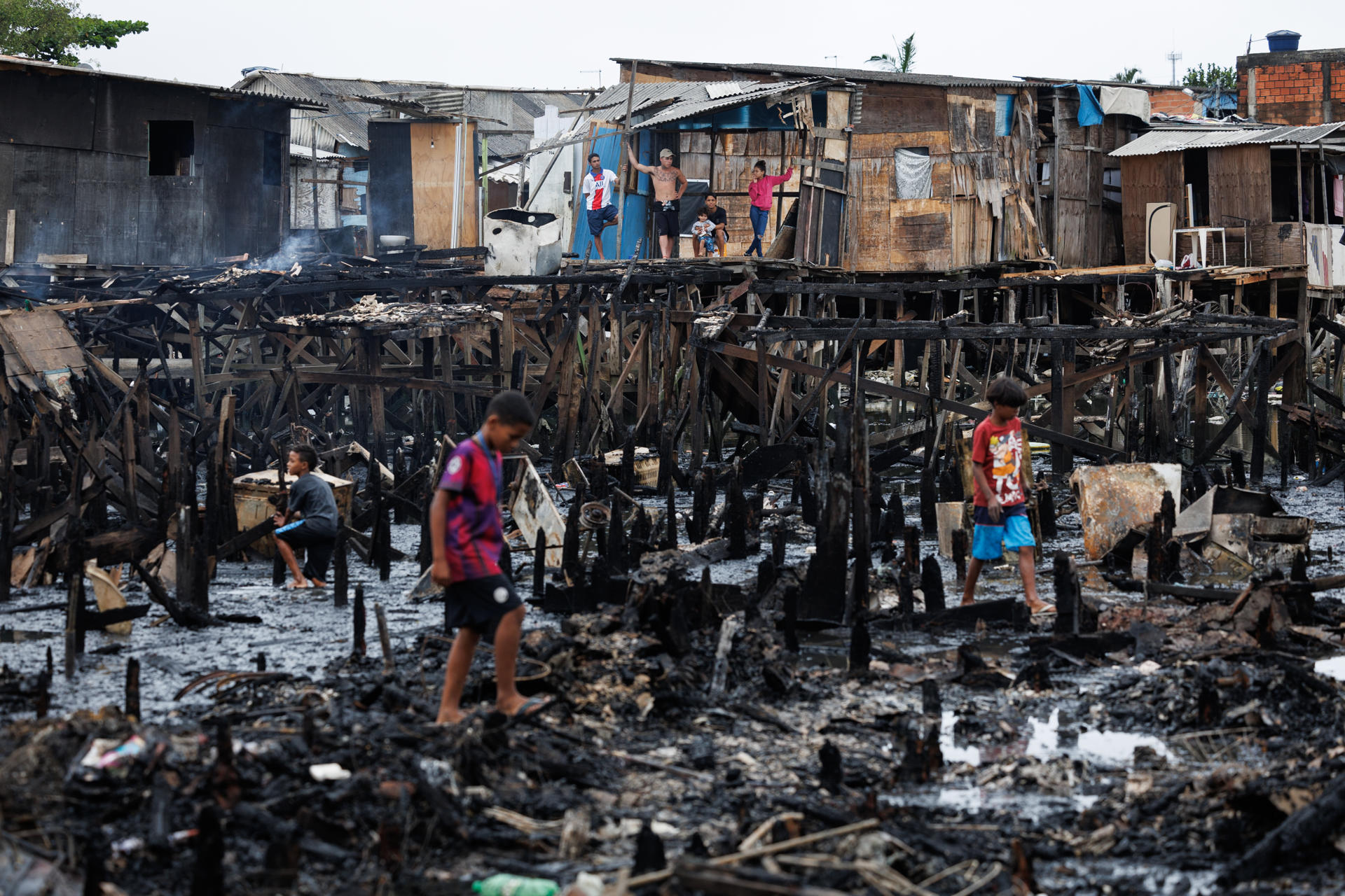 Personas observan los restos y buscan objetos tras un incendio de grandes proporciones que destruyó más de 100 viviendas de madera construidas sobre palafitas, hoy en Santos (Brasil). EFE/Isaac Fontana