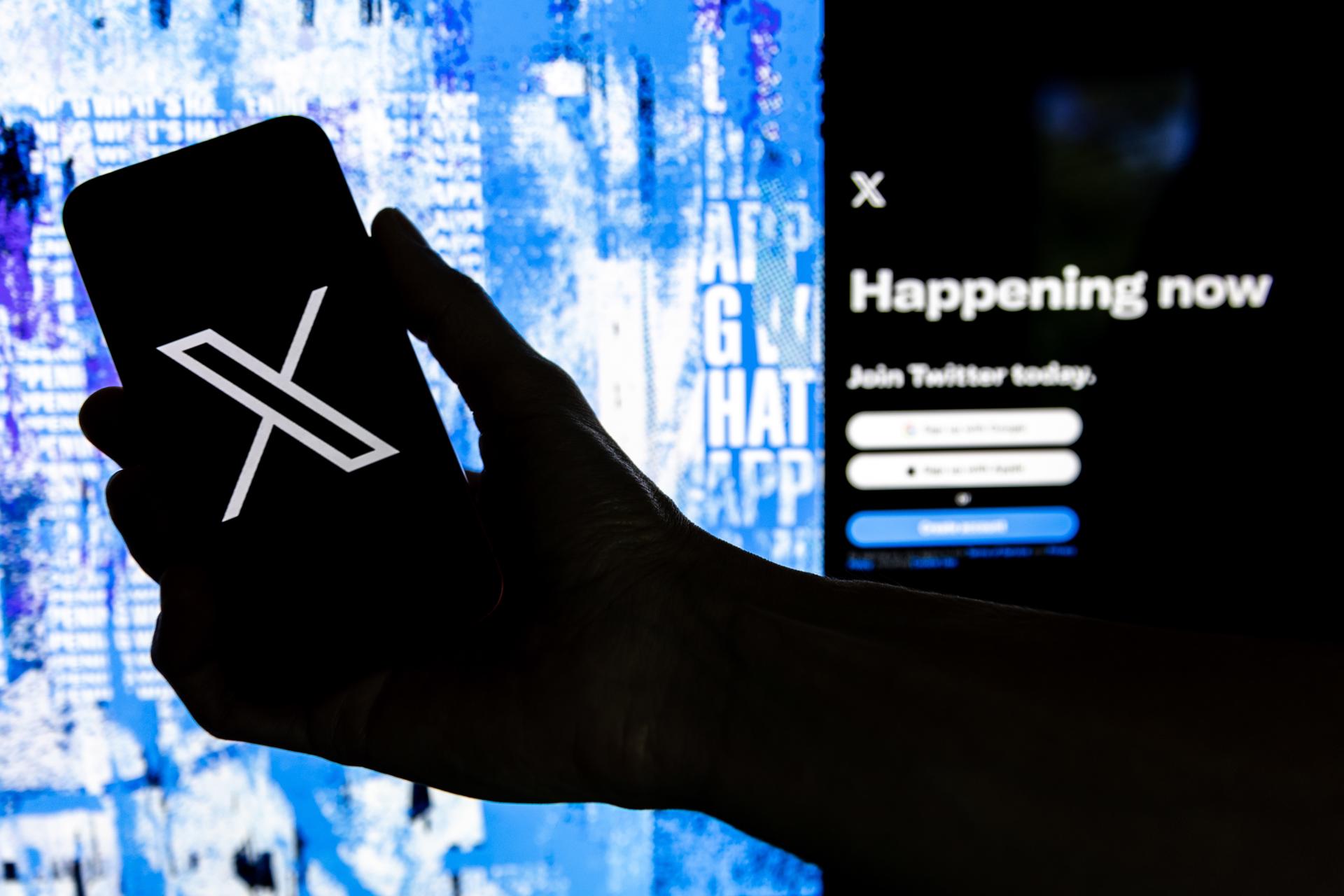 Fotografía de archivo que muestra un usuario mientras sostiene un teléfono móvil que muestra el logotipo 'X' frente a la página principal de la red social. EFE/Etienne Laurent