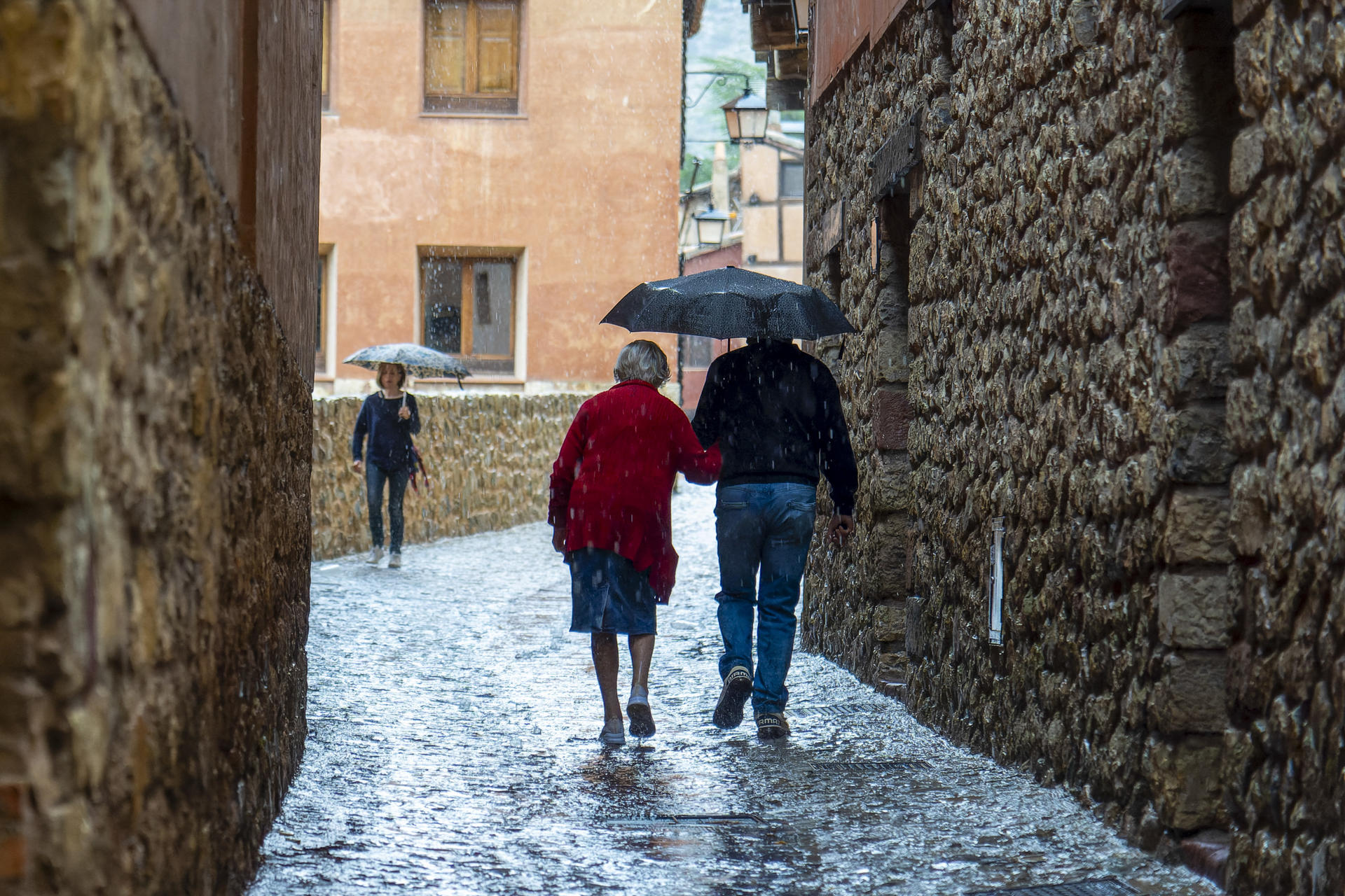 Varias personas caminan por una calle de Albarracín (Teruel) bajo la lluvia. EFE/Antonio Garcia