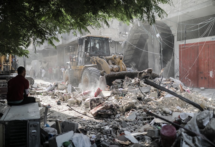 Un hombre observa mientras una excavadora retira los escombros de un edificio residencial que fue arrasado tras un ataque aéreo israelí en Gaza