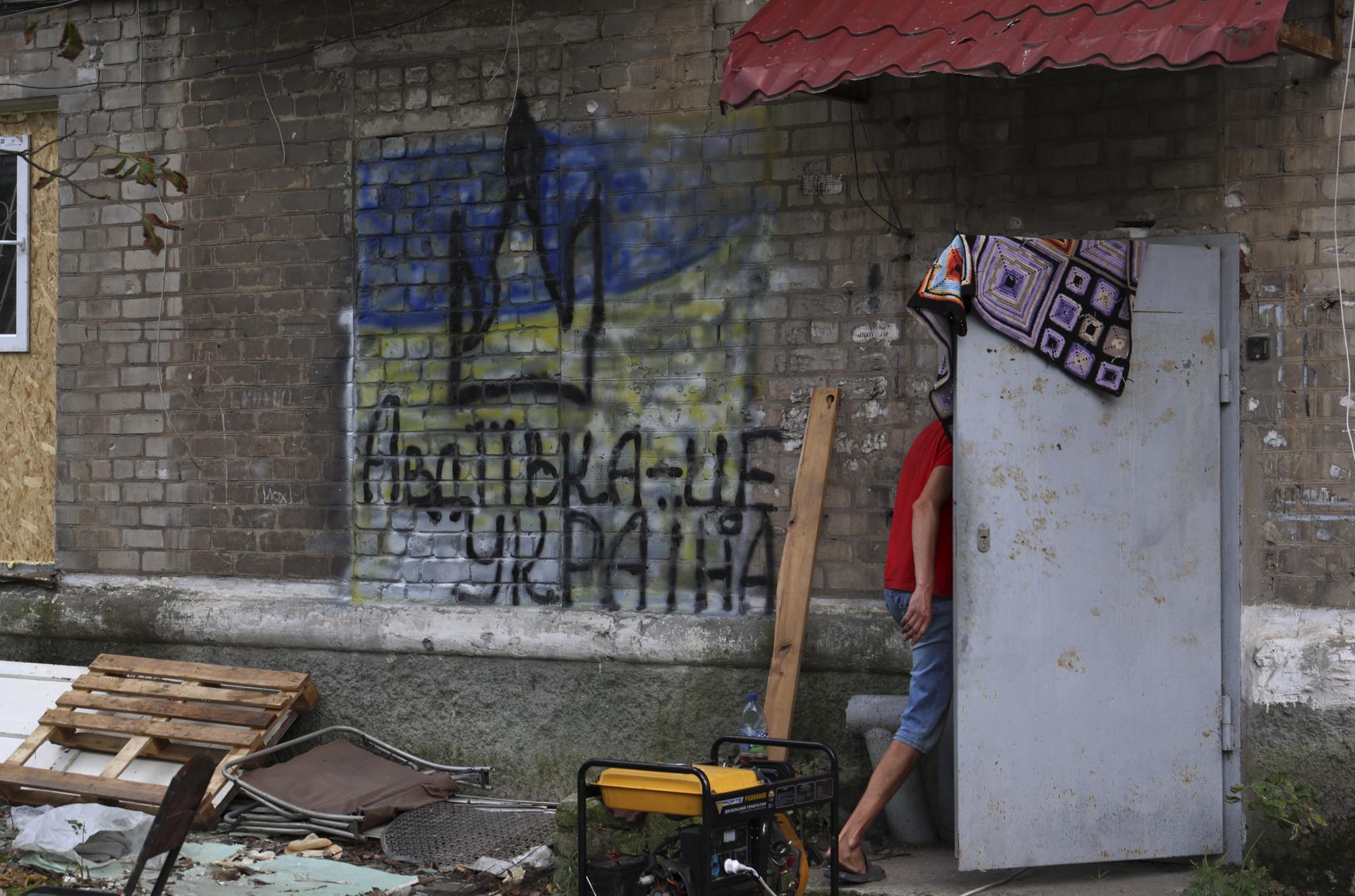 A local man walks through a door next to a wall writing reading 'Avdiivka is Ukraine!' in Avdiivka settlement near a frontline in Donetsk region, Ukraine, 28 August 2023. EFE-EPA FILE/ALEX BABENKO
