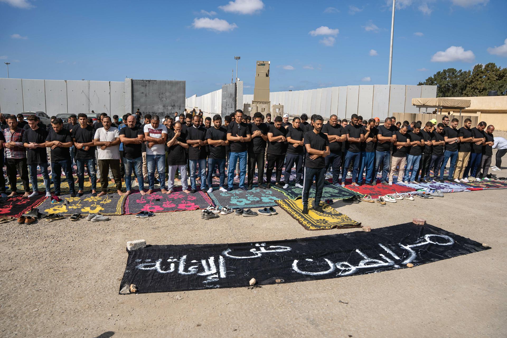 Volunteers from humanitarian aid organizations pray next to a banner reading in Arabic 'stationed until relief delivered' during a sit-in outside Rafah border gate, Egypt, 18 October 2023. EFE-EPA/ALI MOUSTAFA