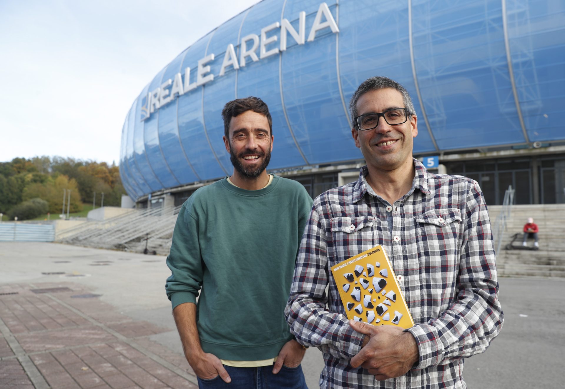 Zuhaitz Gurrutxaga (i) junto al escritor Ander Izagirre con su libro "Subcampeón", ante el estadio de Anoeta de San Sebastián. EFE/Juan Herrero