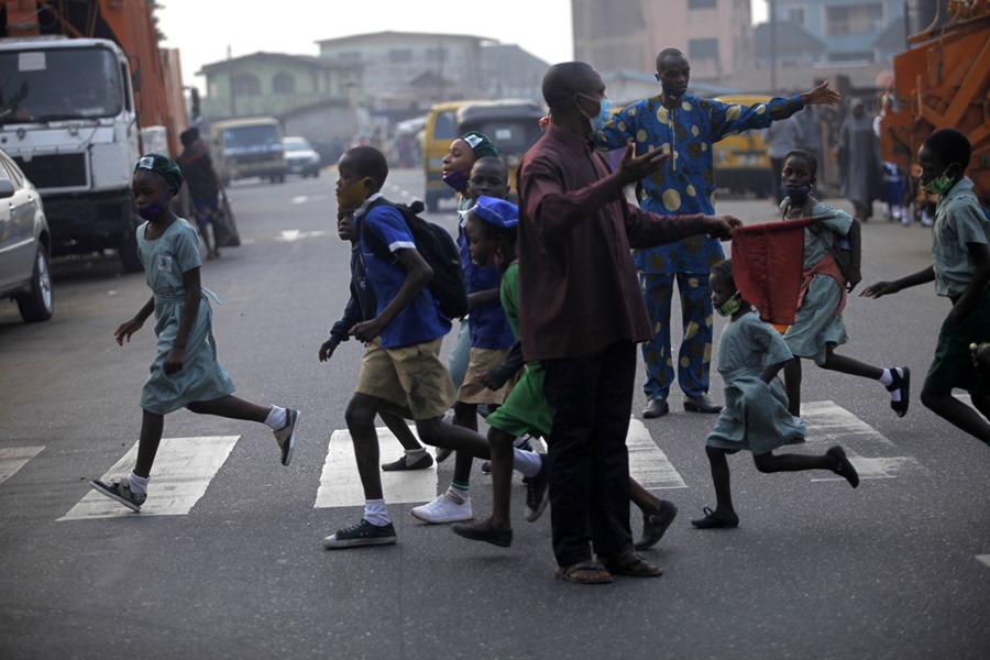 Un hombre dirige el tráfico en un paso de cebra mientras cruzan unos escolares en Lagos