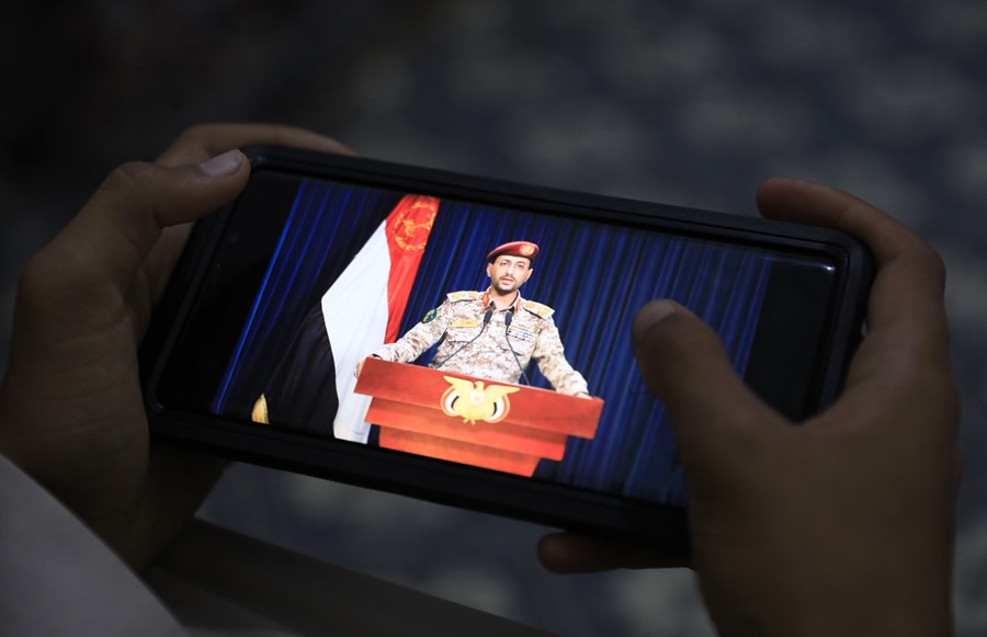 Una persona observa en un teléfono móvil al portavoz militar de los hutíes, Yahya Sarea, pronunciando una declaración televisiva