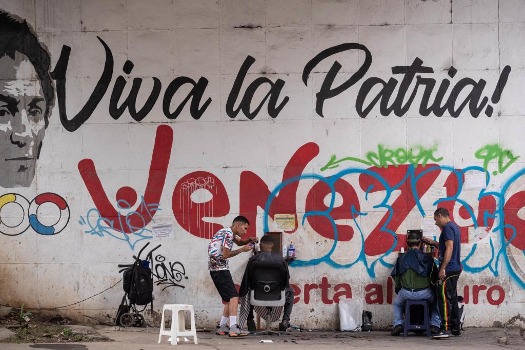 Dos barberos trabajan frente a un mural que dice "Viva la Patria", el 2 de noviembre de 2023, en Caracas (Venezuela). EFE/Rayner Peña R.
