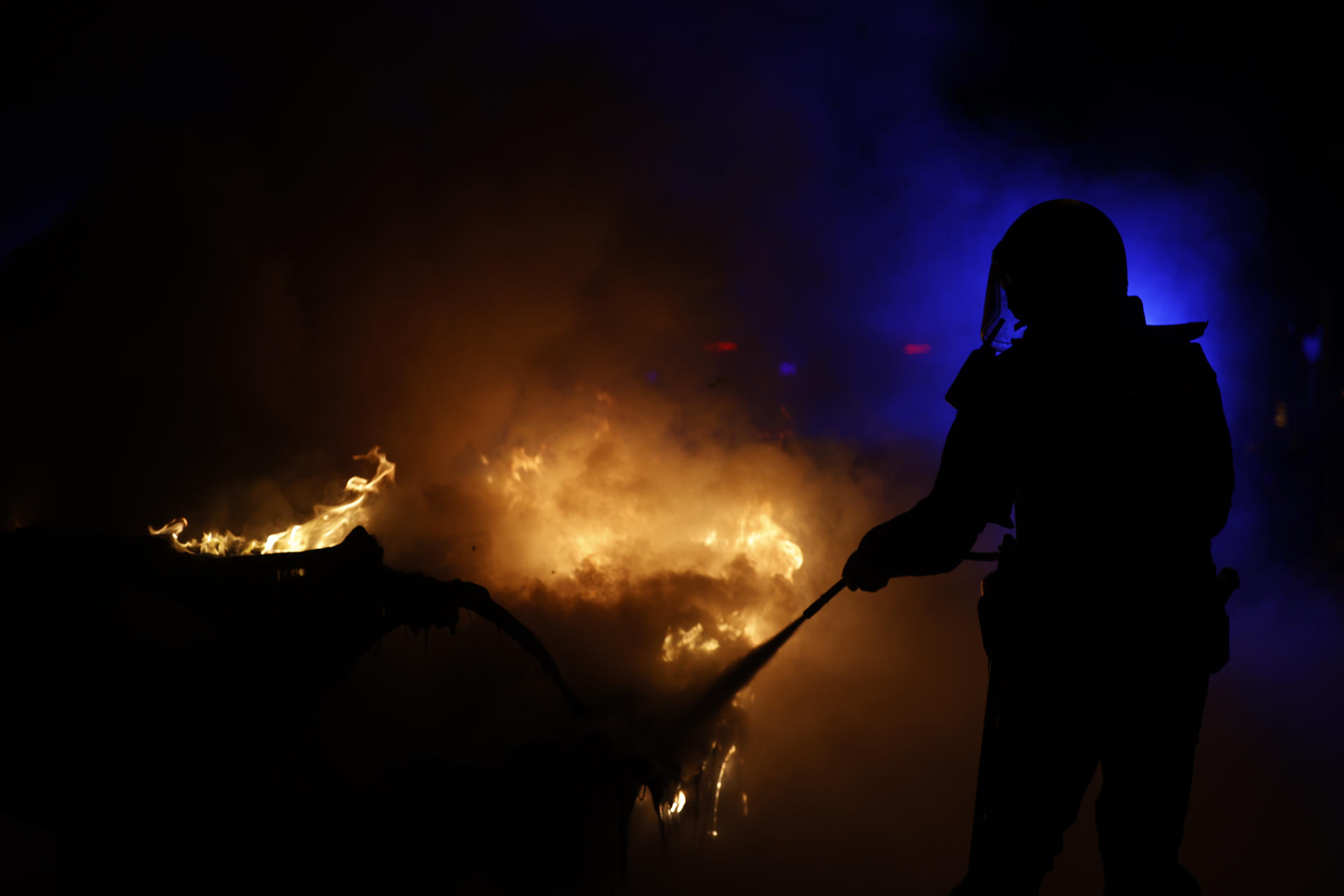 Un policía trata de apagar un contenedor ardiendo en la calle Ferraz, en Madrid, en una nueva jornada de protesta contra la amnistía celebrada este viernes en la capital. EFE/Javier Lizón