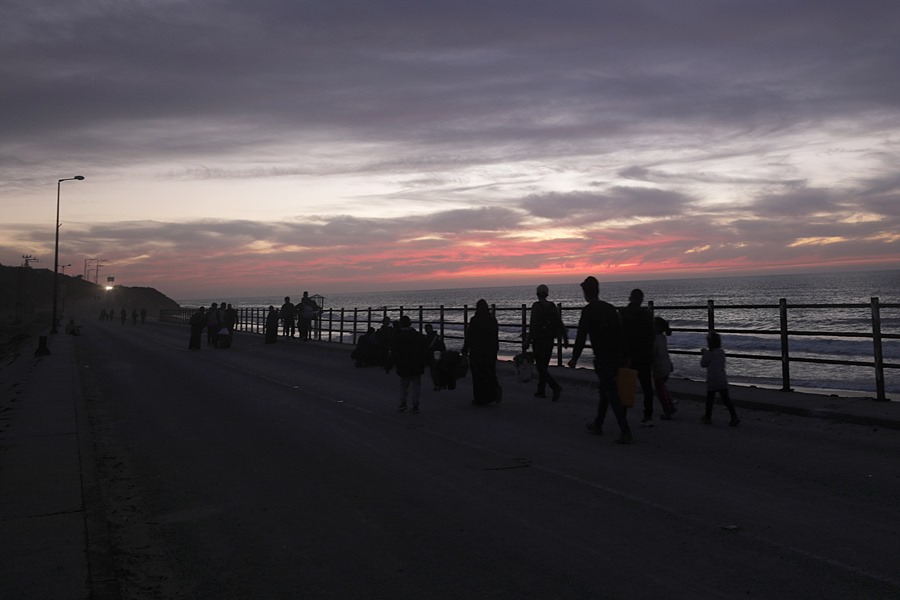 Los palestinos caminan por la carretera costera de Al-Rashid al atardecer después de cruzar del norte al sur de Gaza