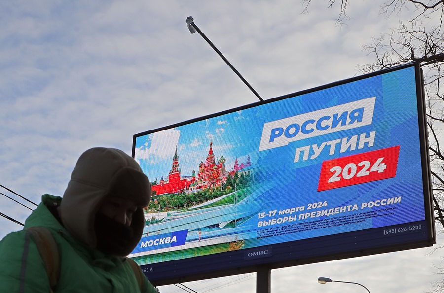 n hombre camina delante de un cartel de la campaña preelectoral que dice "Rusia Putin 2024.