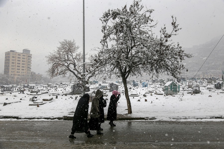 Lugareños caminan junto a un cementerio cubierto de nieve en Kabul, la capital afgana